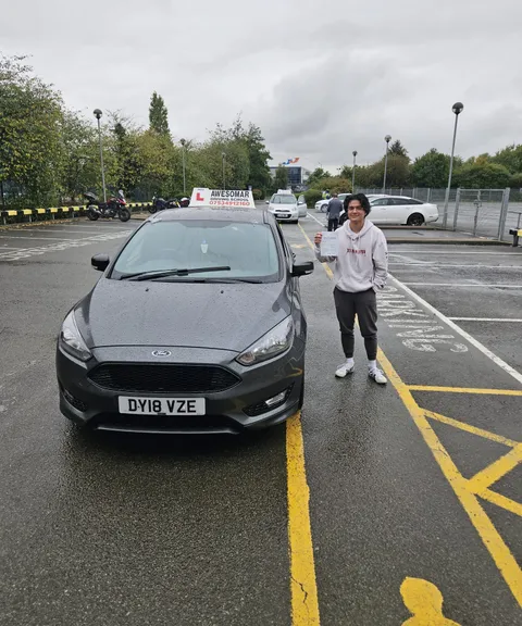 Pupil holding a pass certificate beside the school car on a rainy day
