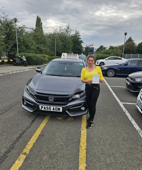 Pupil holding a pass certificate in front of the Awesomar school car